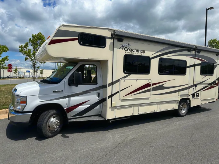 Coachmen Freelander RV rental: A cream and white motorhome with decorative stripes, parked on asphalt, near a stop sign.. Forest River Coachmen Freelander 2018