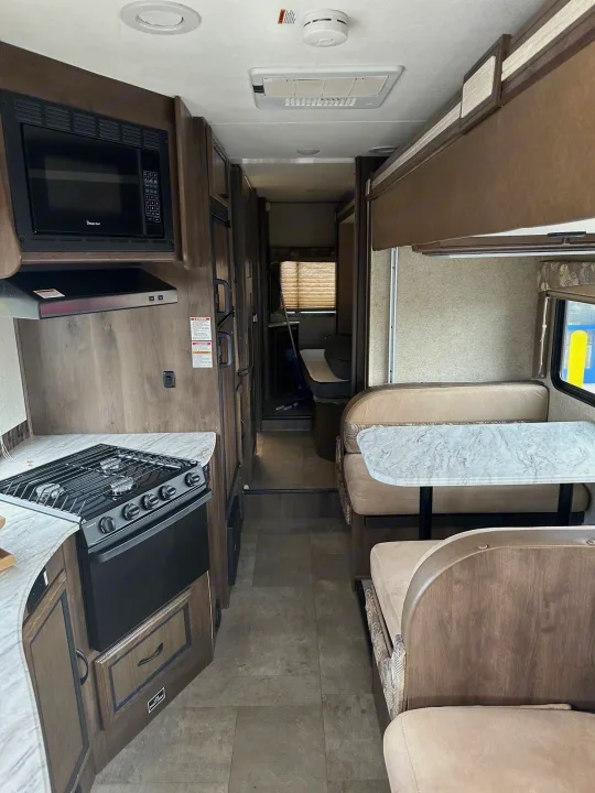 Inside an RV rental: a modern kitchenette with a stove/oven and microwave, plus a cozy dinette.. Forest River Coachmen Freelander 2018