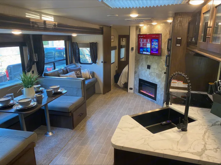Modern RV rental interior showing a full kitchen, dining area, comfy living room with TV/fireplace, and cozy bedroom.. Forest River Cherokee Grey Wolf 2021