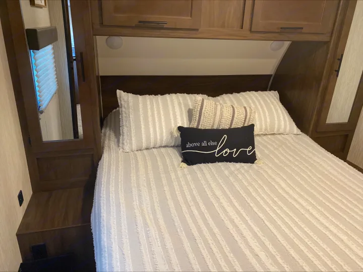 Comfortable RV rental bedroom featuring striped bedding, decorative pillows, and built-in wood cabinetry.. Forest River Cherokee Grey Wolf 2021