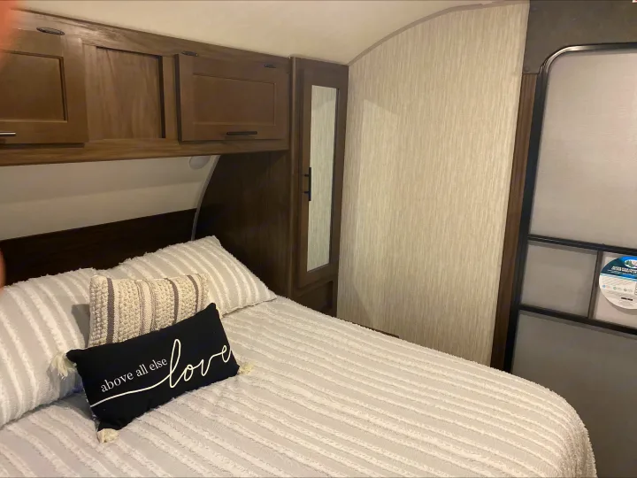 Cozy RV rental bedroom features a striped bedspread, decorative pillows, wooden cabinets, and a mirrored closet.. Forest River Cherokee Grey Wolf 2021