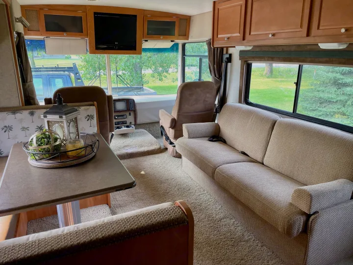 Inside a spacious RV rental: a beige sofa, dinette table, front captain's chairs, and light carpet create a cozy travel space.. Itasca Sunstar 2008