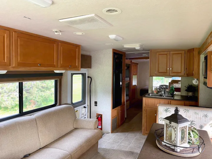 Clean RV rental interior: beige sofa, kitchenette, dining area, and bunk beds visible in the bright space.. Itasca Sunstar 2008