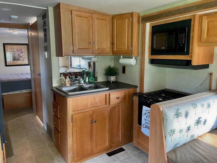RV rental kitchen area: Features a double sink, stovetop, microwave, and dinette. Bedroom access seen beyond.. Itasca Sunstar 2008