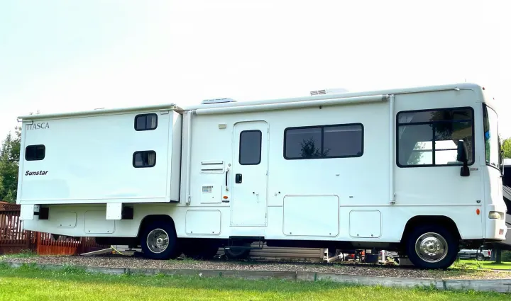 A large white Itasca Sunstar RV rental with its slide-out extended is parked on grass and gravel, ready for travel.. Itasca Sunstar 2008