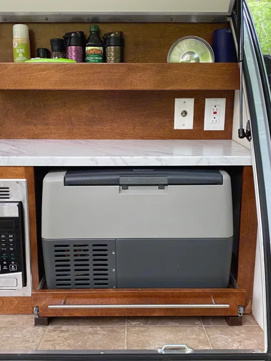 Compact RV rental kitchen with pull-out Norcold fridge, microwave, and organized shelving for essentials.. nuCamp T@G 2019