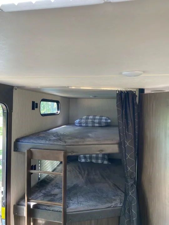 Inside an RV rental: two cozy bunk beds with soft blankets and pillows, plus a window view.. Forest River Cherokee Grey Wolf 2021