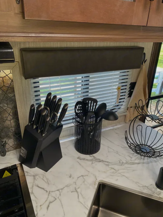 RV rental kitchen counter: black knife set, cooking utensils, and decorative baskets on a modern marble countertop by the sink.. Forest River Cherokee Grey Wolf 2021