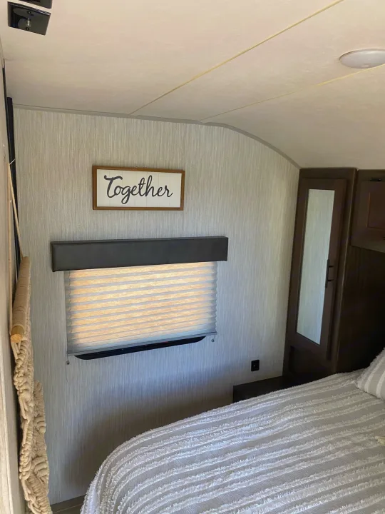 Cozy RV rental bedroom features a textured bed, window blinds, "Together" sign, and built-in storage.. Forest River Cherokee Grey Wolf 2021