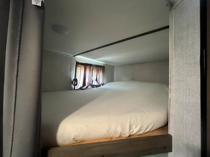 Experience a comfortable night in this compact RV rental bunk bed, featuring white linens and privacy curtains.. Gulf Stream Kingsport 2022