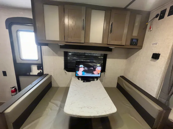 An rv rental interior featuring a dinette table with benches, overhead cabinets, and a flat-screen TV.. Gulf Stream Kingsport 2022