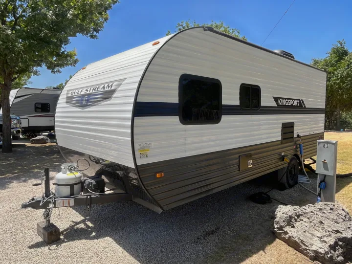 This Gulf Stream Kingsport travel trailer, ideal for your next RV rental, is set up at a sunny campsite.. Gulf Stream Kingsport 2022