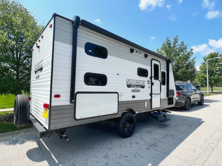 Sunny day shows a gray and white travel trailer RV, hitched to an SUV. Perfect for your next rv rental adventure.. KZ Sportsmen 191BHK 2022