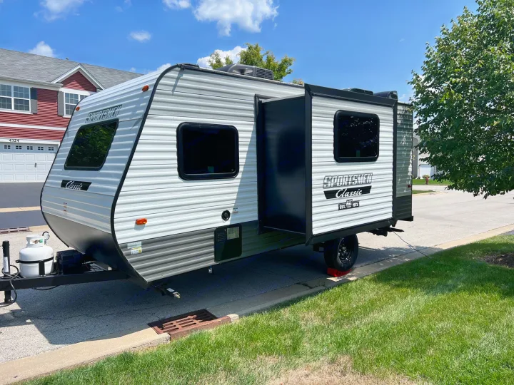 A clean white and black travel trailer, perfect for an rv rental, parked curbside on a sunny residential street.. KZ Sportsmen 191BHK 2022