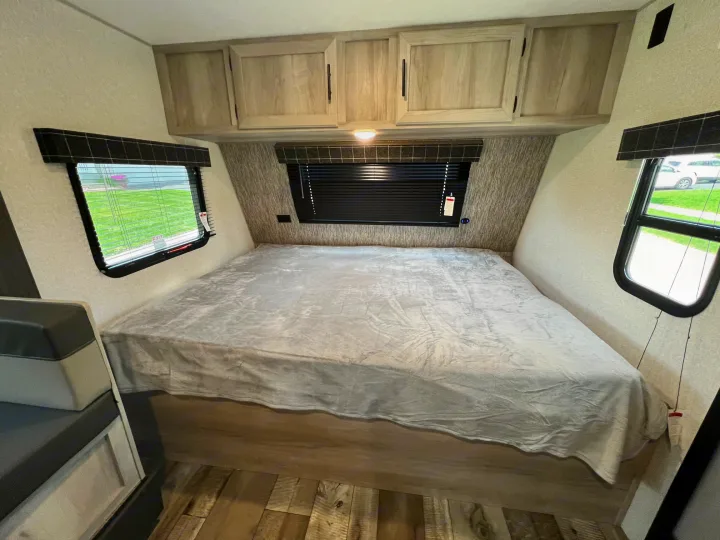 Comfortable RV rental bedroom with a spacious bed, light wood overhead cabinets, and side windows.. KZ Sportsmen 191BHK 2022