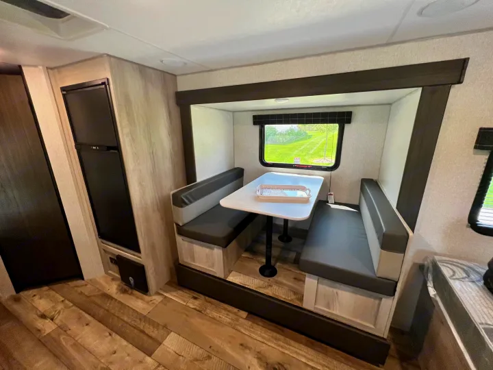 Modern RV rental interior features a cozy dinette with booth seating, table, window view, and a built-in refrigerator.. KZ Sportsmen 191BHK 2022