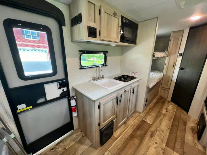 RV rental interior: kitchen counter with sink & stovetop, overhead microwave, and bunk beds. Wood-look floor visible.. KZ Sportsmen 191BHK 2022