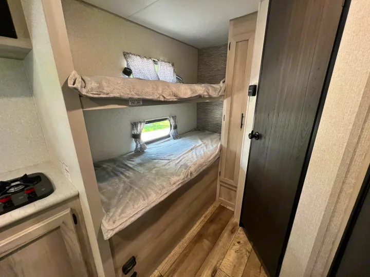 Compact RV rental interior featuring stacked bunk beds with windows, plus a glimpse of the kitchen area.. KZ Sportsmen 191BHK 2022