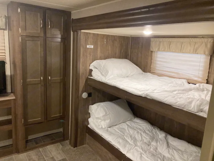 RV rental interior: bunk beds with white bedding, wooden cabinets, and tiled flooring create a functional sleeping area.. Palomino Puma 31DBTS 2020