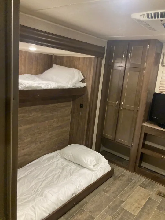 Cozy RV rental interior: bunk beds with white linen, wood-paneled walls, a built-in wardrobe, and TV area.. Palomino Puma 31DBTS 2020