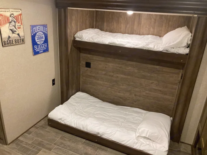 Cozy RV rental interior featuring comfortable bunk beds with white bedding and classic baseball decor, perfect for family travel.. Palomino Puma 31DBTS 2020