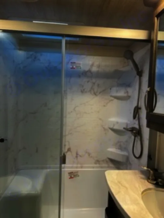 Modern shower within an RV rental, featuring a clear glass shelf, marble-look walls, and dual showerheads for comfort.. Keystone RV Cougar 2022
