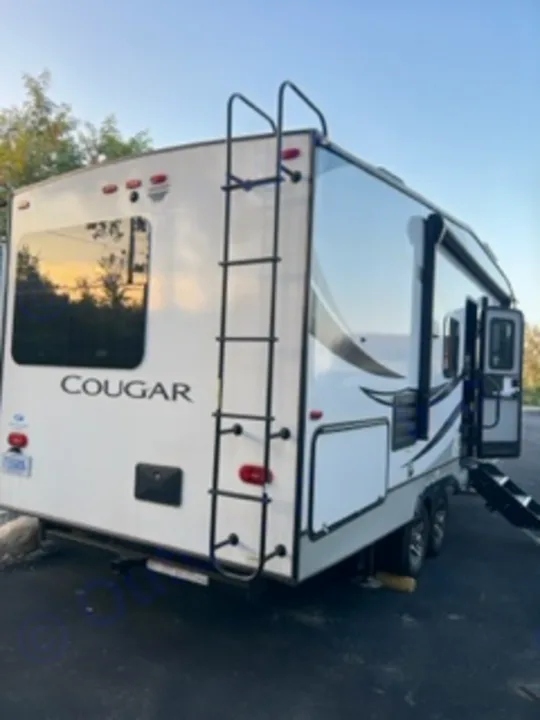 A white Cougar travel trailer, seen from the rear with a ladder and storage hatches, ready for your next RV rental adventure.. Keystone RV Cougar 2022