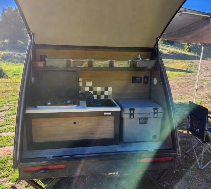 RV rental teardrop camper outdoor kitchen. View inside the rear hatch with stove, sink, cooler, and storage. Perfect for camping.. Braxton Creek Bushwacker 2023