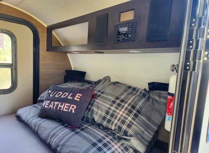 Cozy RV rental bedroom with plaid bedding, 'CUDDLE WEATHER' pillow, and overhead entertainment system. Ideal for travel.. Braxton Creek Bushwacker 2023