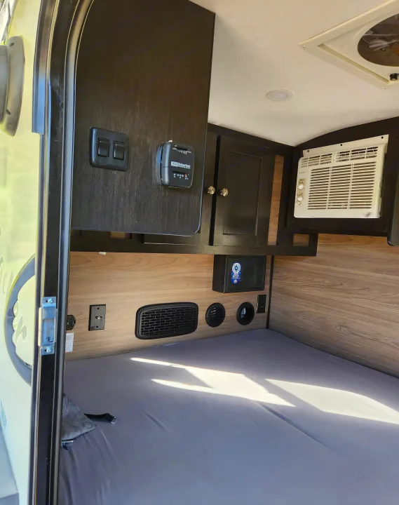 RV rental interior view: compact sleeping area with an AC unit, thermostat, and storage cabinetry clearly visible.. Braxton Creek Bushwacker 2023