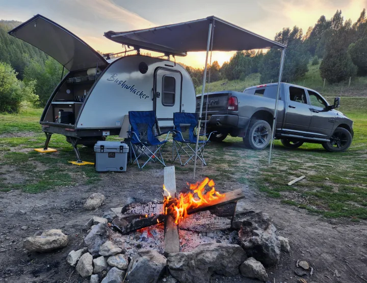 Cozy RV rental setup: Teardrop trailer, truck, and warm campfire under a sunset sky, perfect for outdoor camping adventure.. Braxton Creek Bushwacker 2023