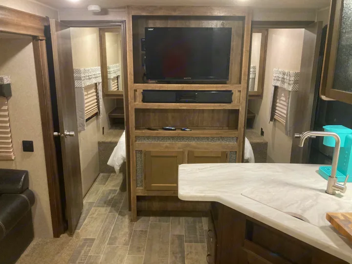 Inside an RV rental: a central entertainment unit faces a living area, with a bedroom beyond, and a kitchen island in the foreground.. Palomino Puma 31DBTS 2020
