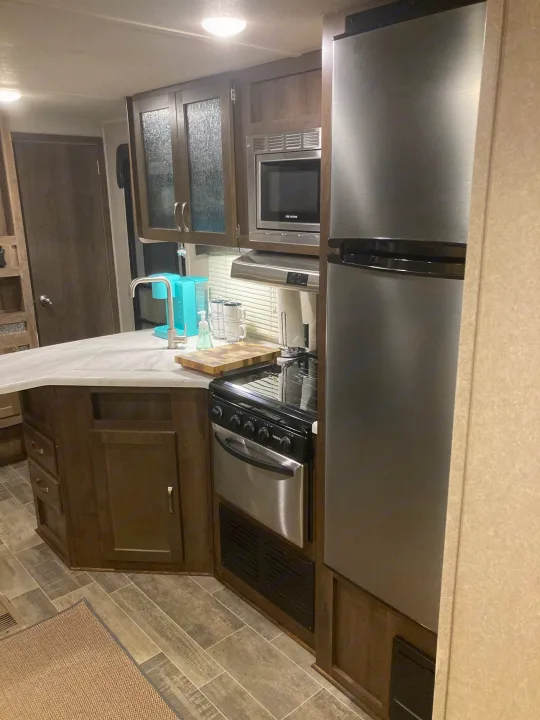 Inside an RV rental: a compact kitchen featuring a large fridge, microwave, stove, and modern sink area with a coffee maker.. Palomino Puma 31DBTS 2020