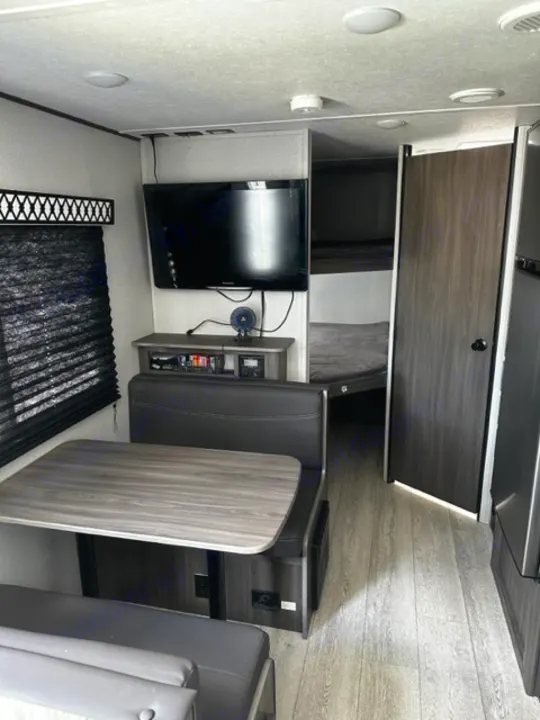 Modern RV rental interior with a wood-grain dinette table, compact kitchen, and wall TV. Functional living space.. Forest River Shasta 2021