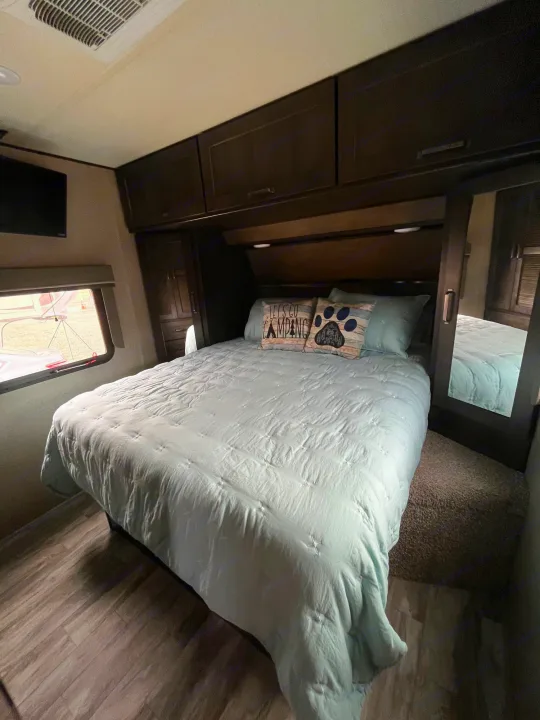 Cozy RV rental bedroom with a queen bed, overhead storage, and TV, ready for your next camping trip.. Grand Design Reflection 2022