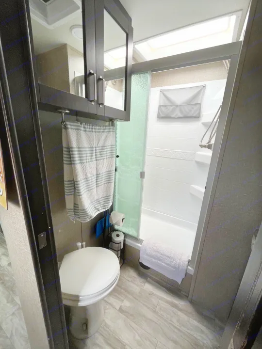 Compact RV rental bathroom featuring a toilet, glass shower, and mirrored cabinet. Perfect for travel convenience.. Grand Design Reflection 2022