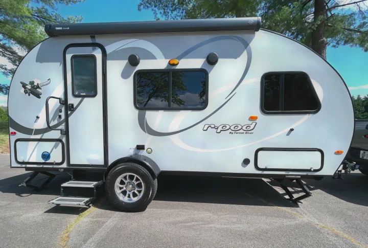 A light gray r-pod travel trailer, an RV rental, is parked on asphalt with steps deployed. It features an awning, door, and windows.. Forest River R-Pod 2021
