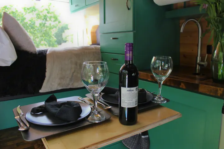 An RV rental interior featuring a table set for two with a bottle of CK Mondavi wine, glasses, and dinnerware.. Ford Transit 2017