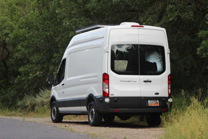 White Ford Transit 250 camper van with solar panels for RV rental, parked roadside by green trees.. Ford Transit 2017