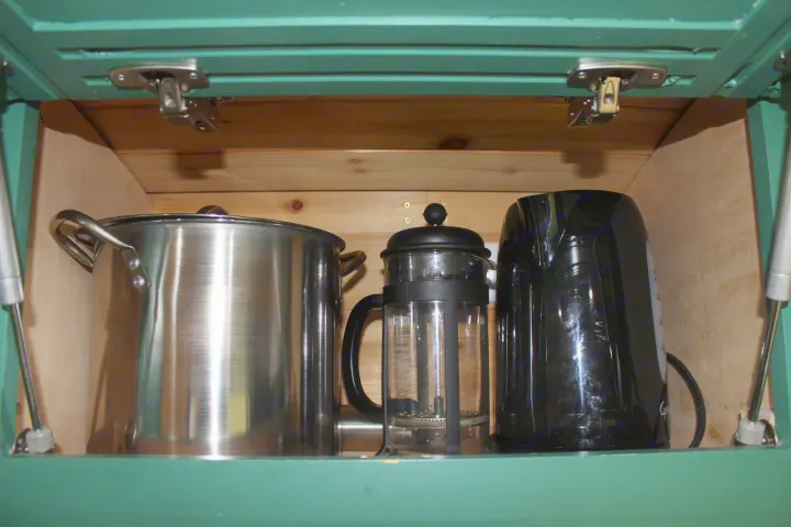 RV rental kitchen cabinet showing a stainless pot, glass French press, and black electric kettle for convenient cooking and coffee.. Ford Transit 2017