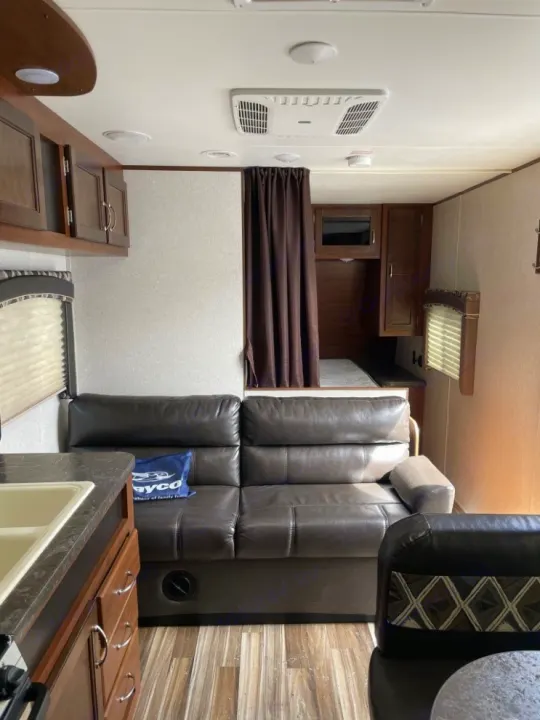 Modern RV rental interior showcasing a comfortable brown sofa, full kitchen, and a separate bedroom behind curtains.. Jayco Jay Flight 2017