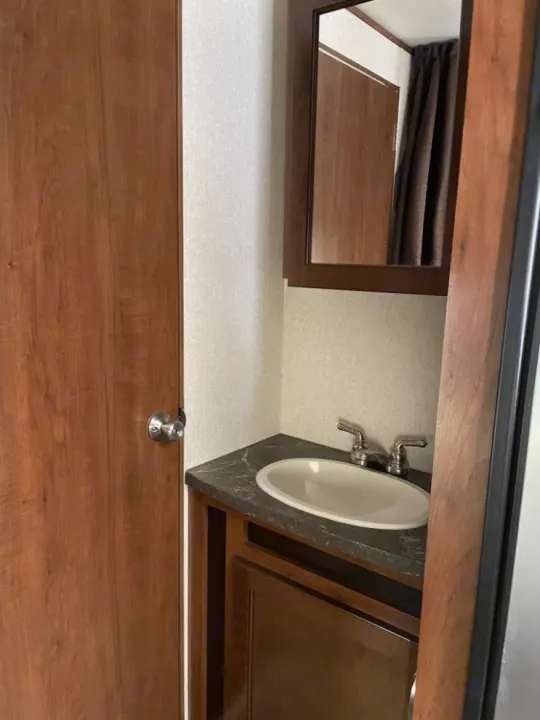 RV rental bathroom interior: A wooden door on the left, leading to a vanity with a sink and mirror on the right.. Jayco Jay Flight 2017