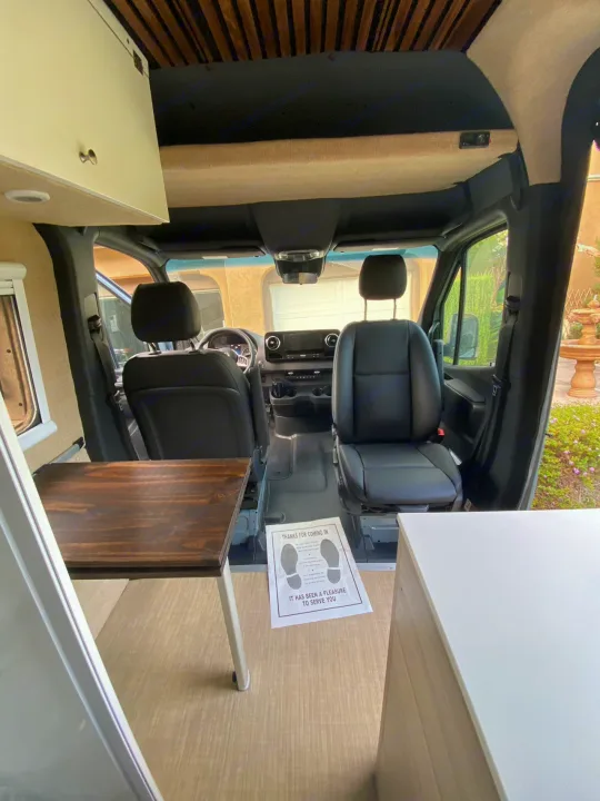 Spacious camper van interior, perfect for rv rental adventures. Features swiveling seats & wooden table for versatile living.. Mercedes Benz Sprinter 2500 2022
