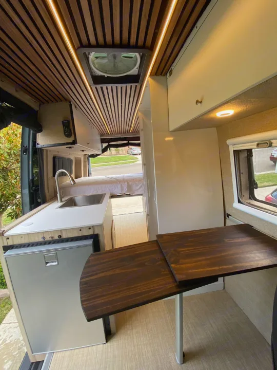 Explore this stylish RV rental interior, showcasing a modern kitchen, comfortable bed, and versatile dining space.. Mercedes Benz Sprinter 2500 2022