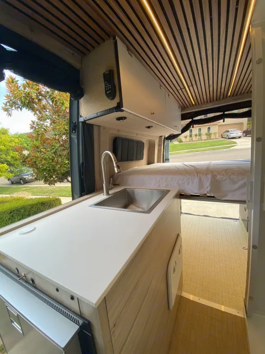 Stylish RV rental interior: modern camper van with functional kitchen, sink, bed, and wood-slatted ceiling.. Mercedes Benz Sprinter 2500 2022