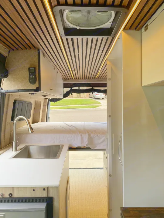 RV rental interior featuring a stylish kitchenette, cozy bed, and custom wood-slatted ceiling with accent lights.. Mercedes Benz Sprinter 2500 2022