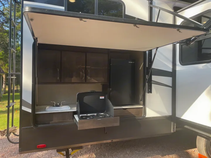 This RV rental features a convenient outdoor kitchen with a sink, pull-out stove, mini-fridge, and overhead cabinets.. Grand Design Reflection 2022