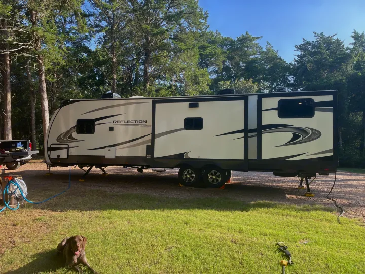 Relaxing RV rental adventure: a Grand Design Reflection travel trailer fully set up at a wooded campsite with a dog.. Grand Design Reflection 2022