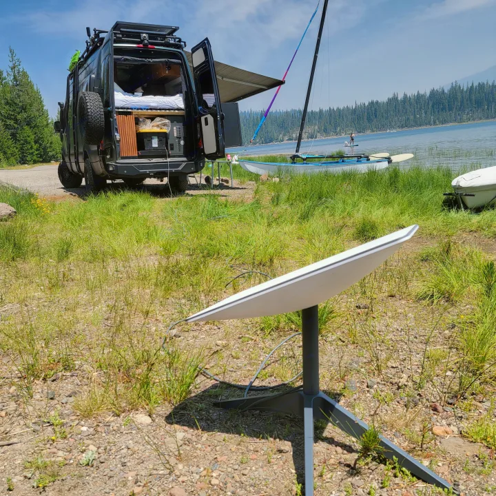 Black RV rental van with open doors and a Starlink dish set up by a serene lake, ideal for remote work and camping.. Mercedes-Benz Sprinter 2020