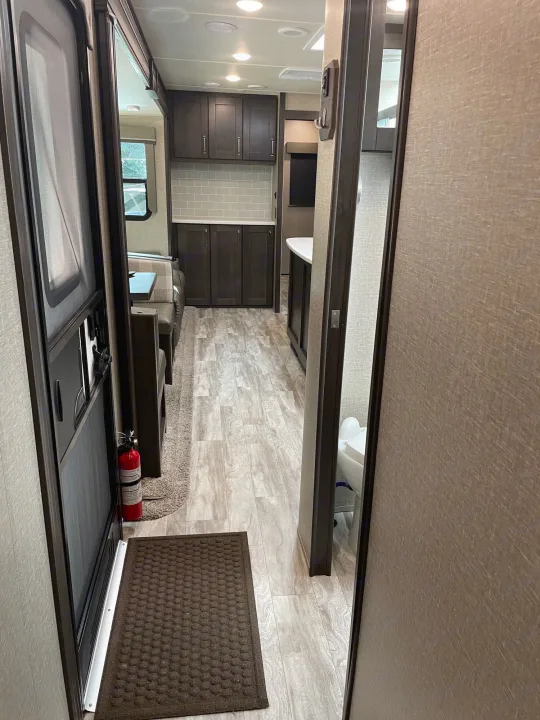 Bright RV rental interior featuring a well-equipped kitchen, dining booth, and hallway leading to the bathroom.. Grand Design Reflection 2022